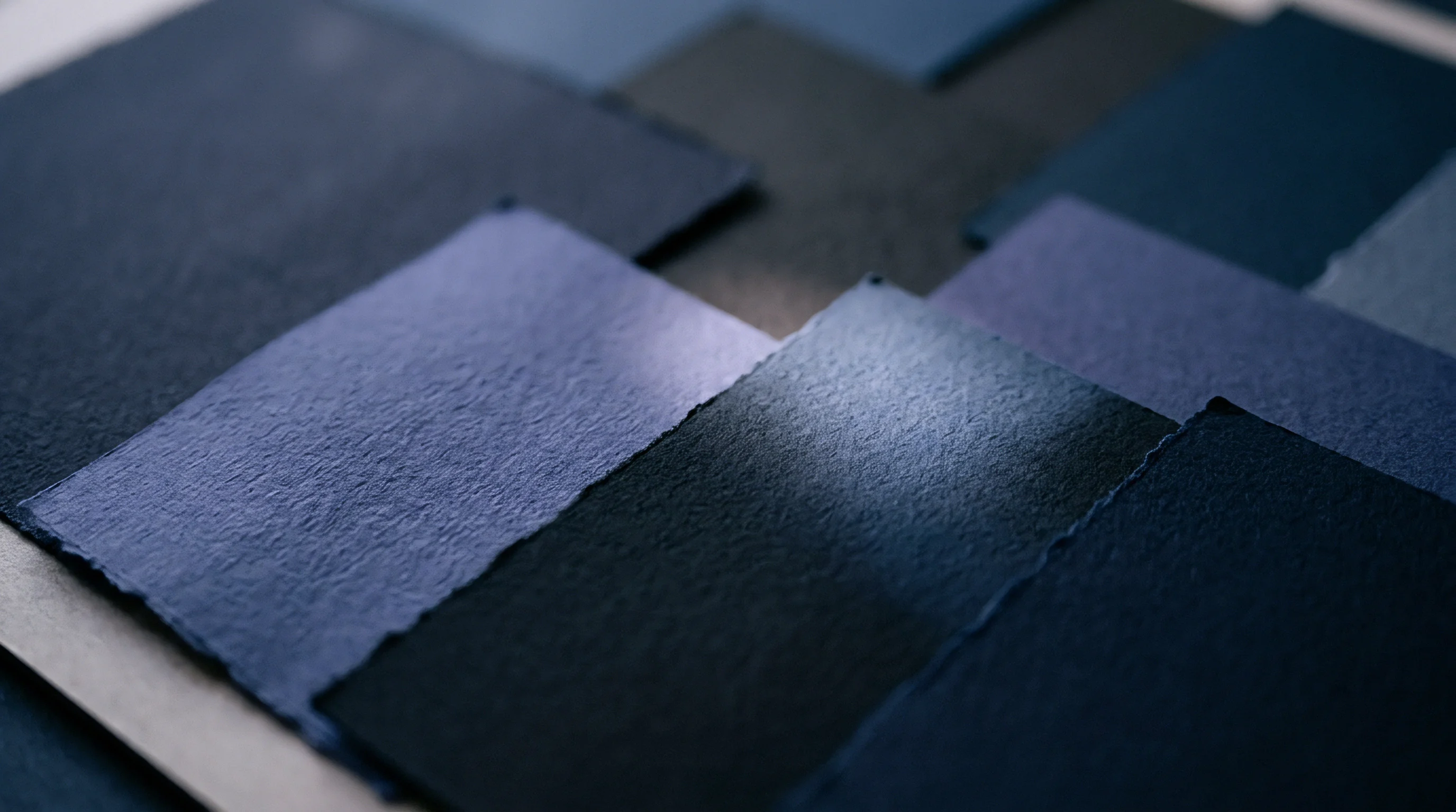 Multiple overlapping rectangular swatches of textured heavy weight paper sit in staggered formation containing dark blue and indigo tonal shifts.