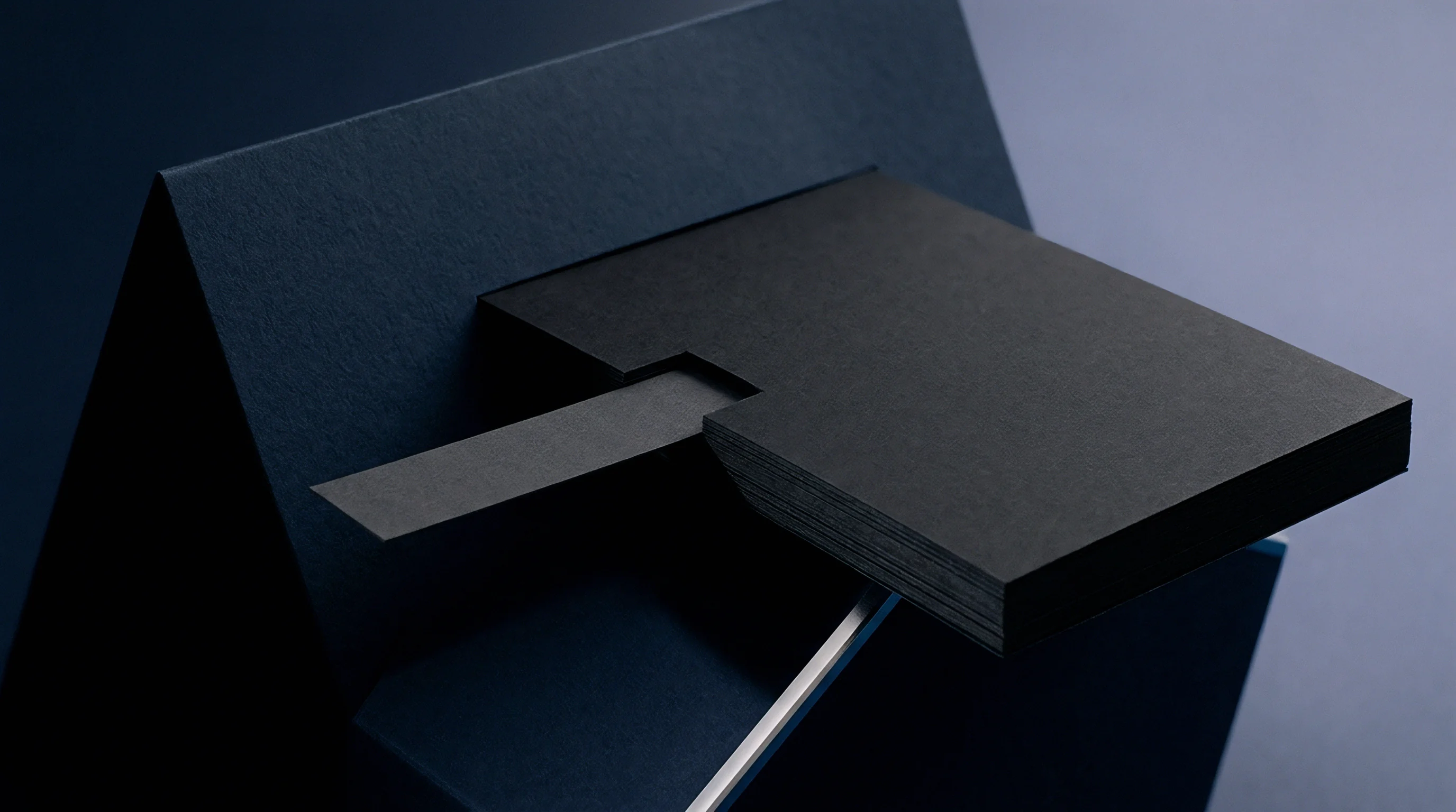 Dark cardstock blocks rest against blue paper sheets with a grey strip inserted between layers of a thick material stack.