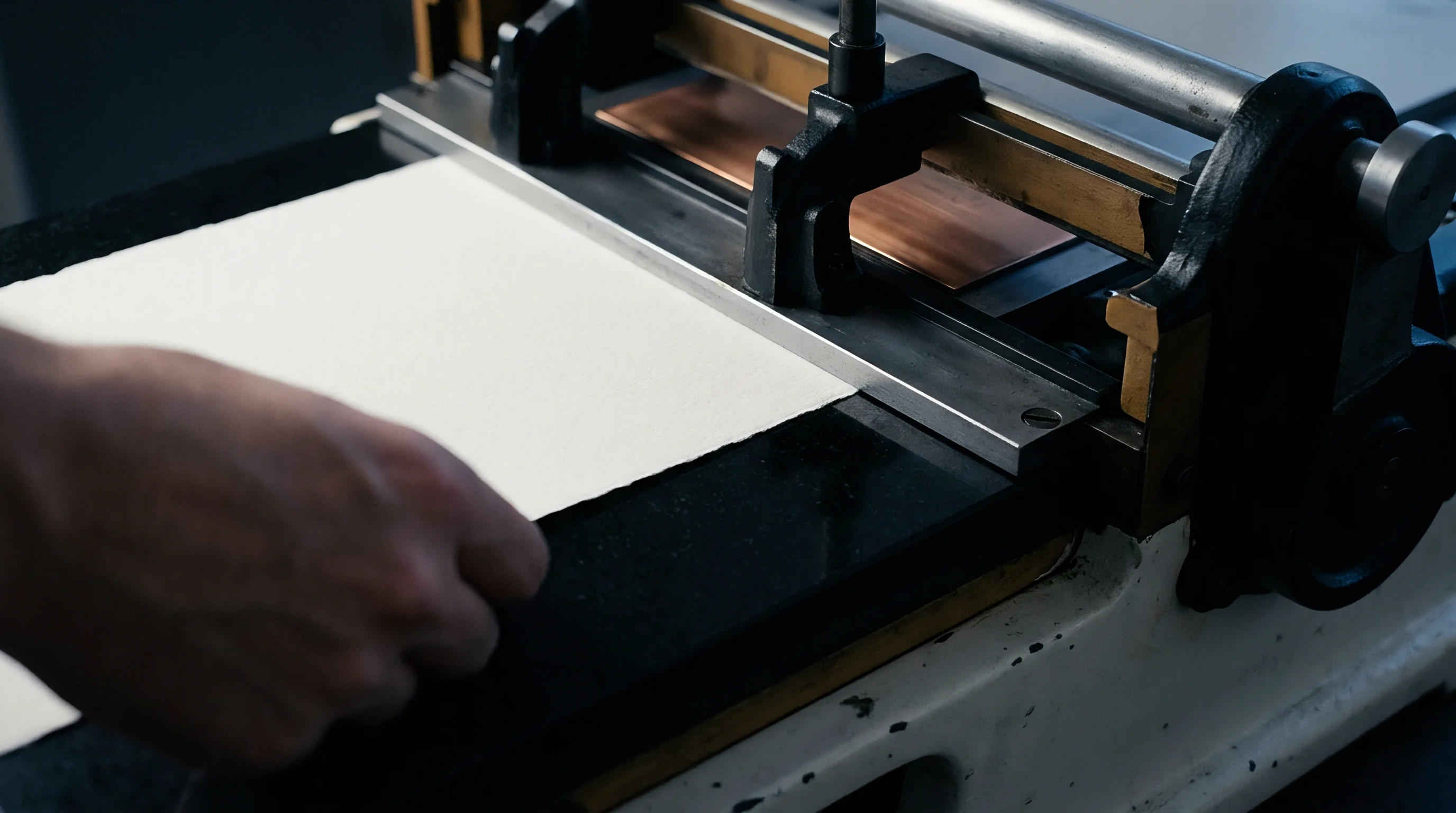 A hand places a heavy white substrate sheet onto the bed of an industrial manual press for precision converting or proofing applications.